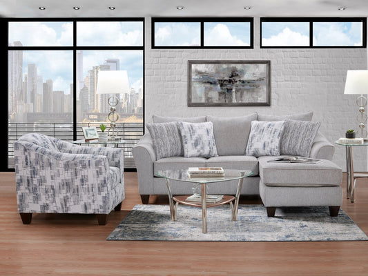 Full living room scene showcasing the entire Spit Ash sofa chaise and a coordinating accent chair, bathed in natural light with a city view.