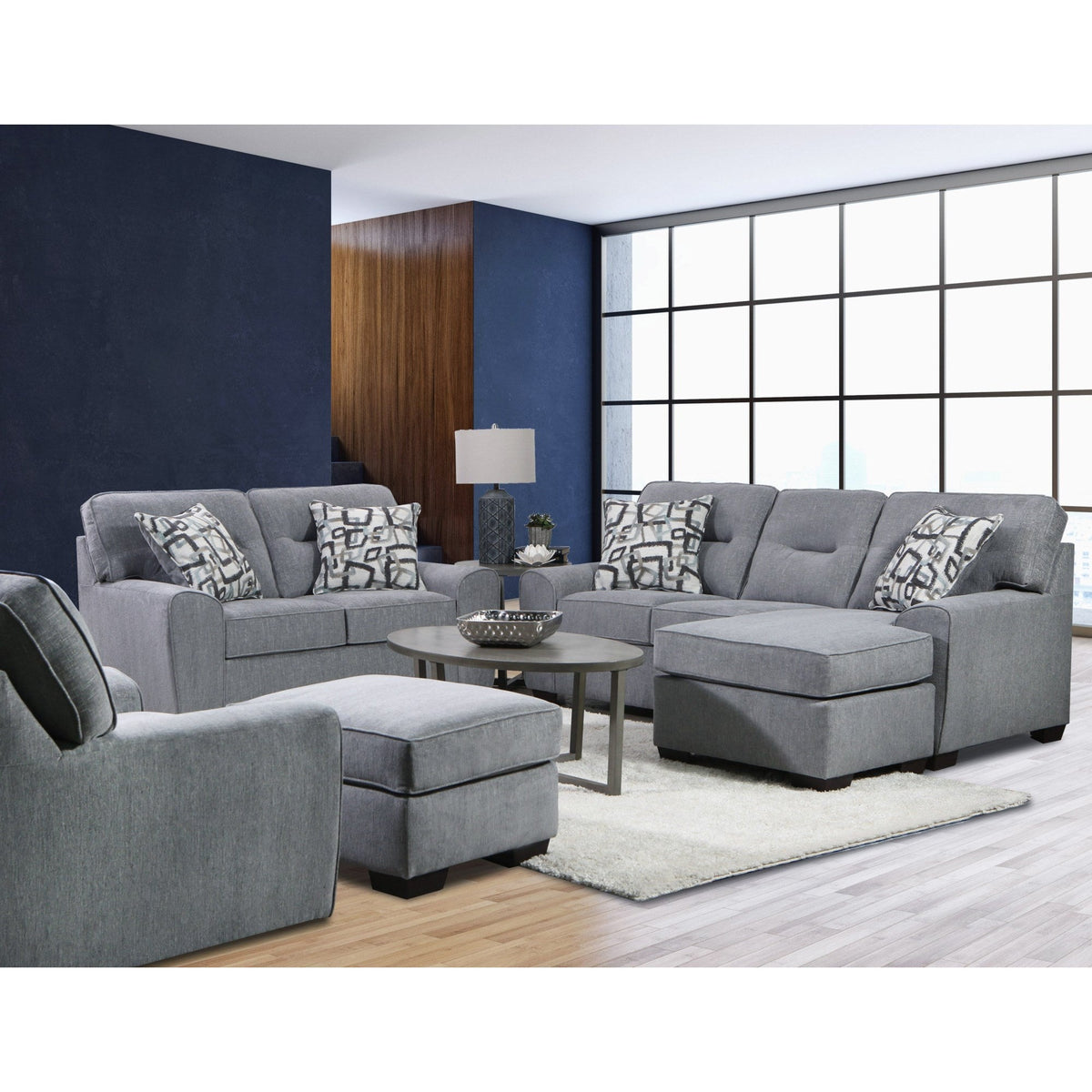 Full view of a dark gray sofa and loveseat set with track arms and geometric throw pillows in a bright, modern living space.
